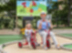 Blippi and a child on red tricycles at "Trike Town" wearing helmets get ready for adventures