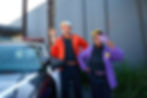 Blippi and Meekah playfully hold magnifying glasses beside a police car.