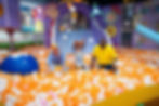 Blippi playing in an orange and white ball pit with a smiling child and adult